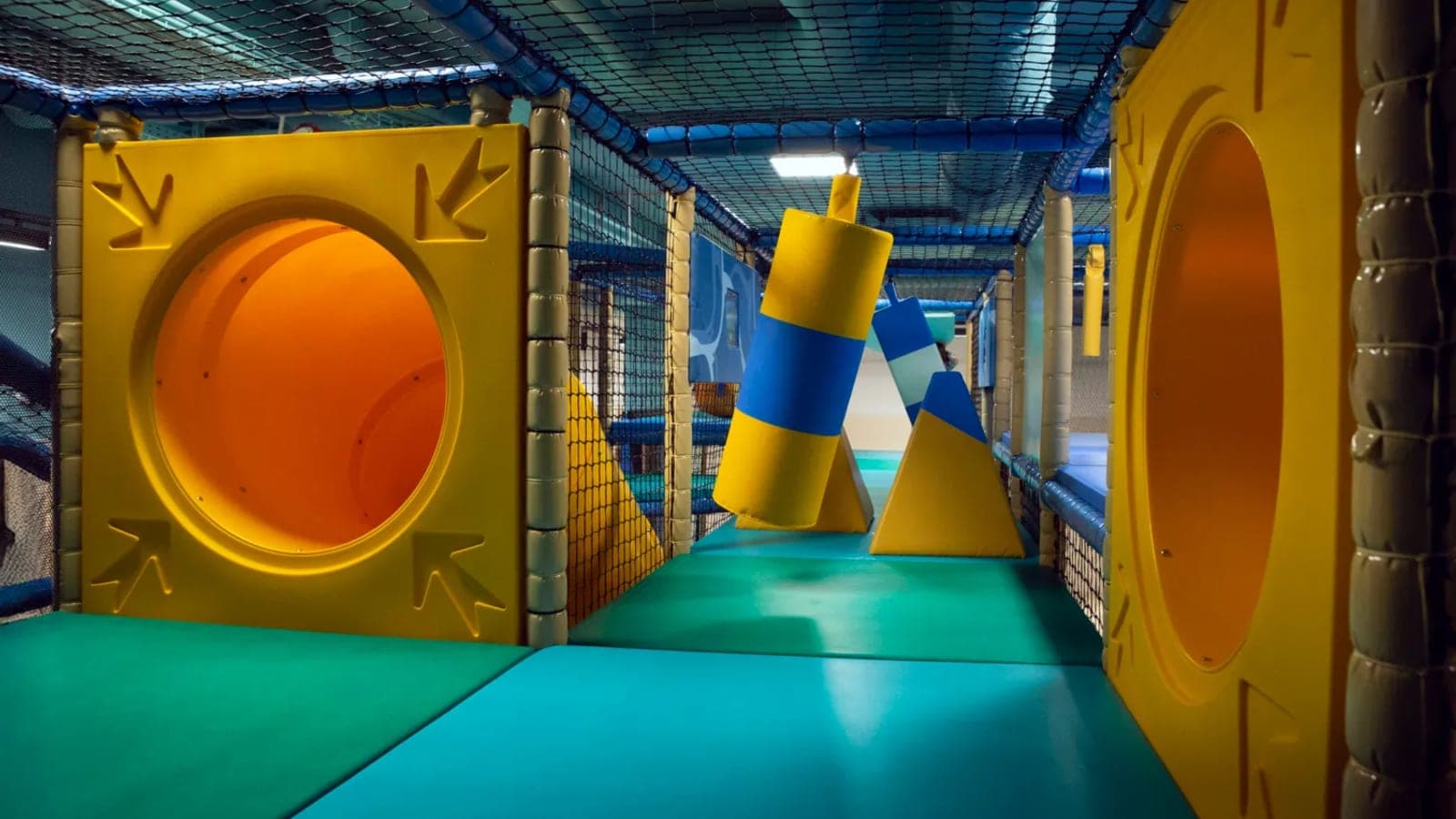 Kidiz Belval soft play interior — padded yellow tunnels with round portholes, blue safety netting and turquoise rubber flooring