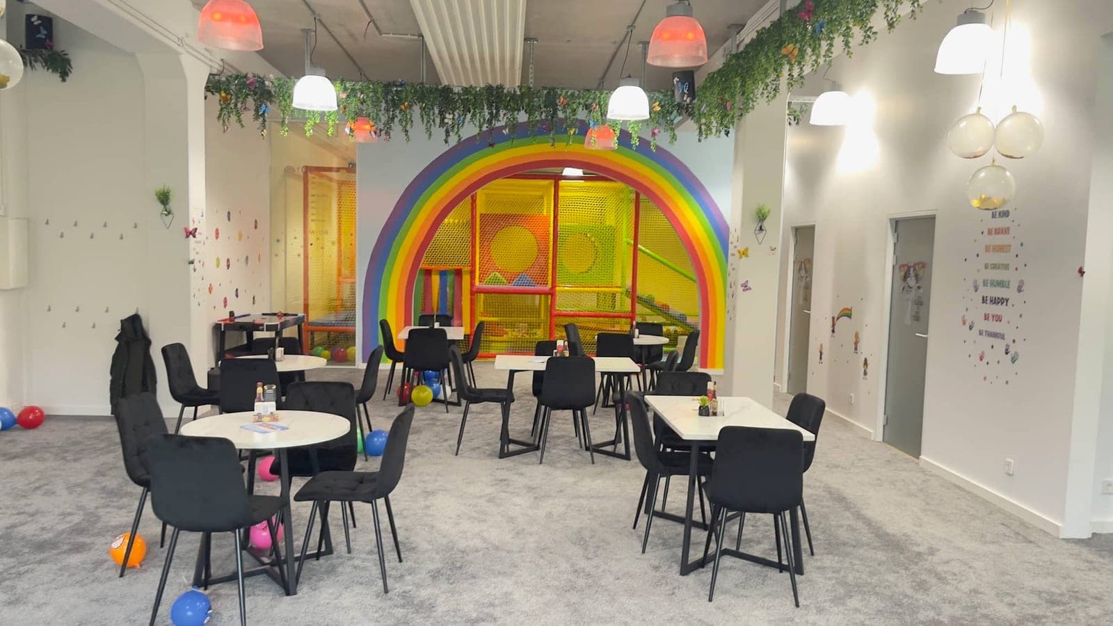 Playground Café interior — café seating with black chairs and white tables in front of the rainbow-arched soft-play structure