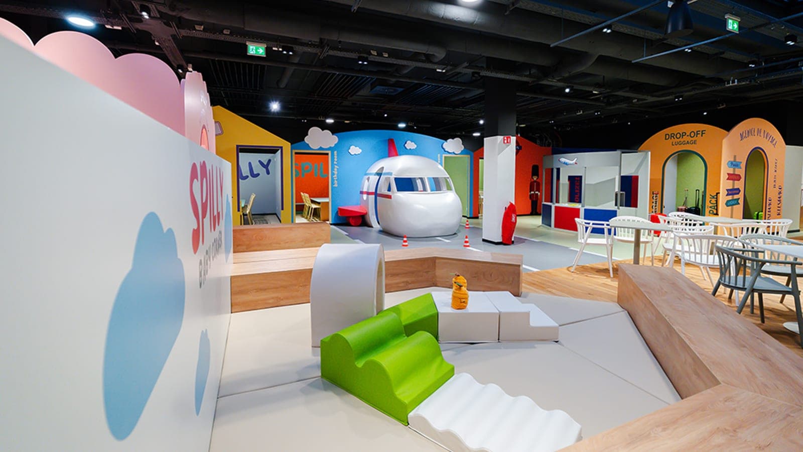 Spilly's central hall — child-sized airplane, SPILLY signage on the cloud-shaped wall, foam play area and rows of parents' seating under skylights